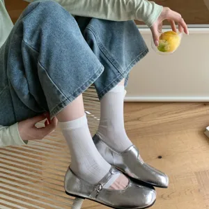 Detail view of stylish silver metallic flat Mary Jane shoes paired with white socks for women.