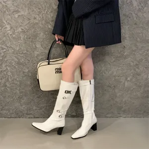 Detalle de botas altas blancas de cuero charol con multiples hebillas y tacón estilo.