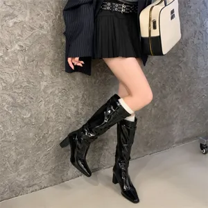 Botas altas negras de charol con tacón ancho, punta puntiaguda y elegante diseño de hebilla.