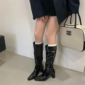 Botas altas decharol negro con tacón ancho, puntera puntiaguda y elegantes correas con hebillas.