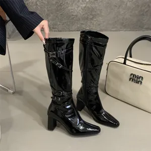 Detalle en primer plano de botas altas de charol negro con correas de hebilla y tacón ancho.