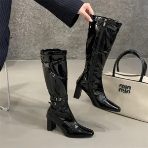 Vista detallada de unas bonitas botas altas de charol negro con tacón grueso y hebillas.