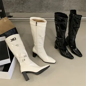 Vista detallada de botas altas de charol con punta puntiaguda, tacón grueso y tiras con hebilla.