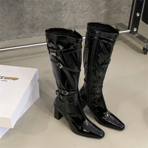 Botas altas de charol negro con elegantes correas de hebilla y tacones gruesos.