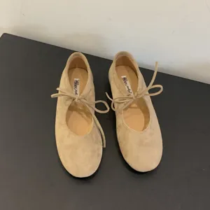 Close-up view of beige suede ballet flats with delicate lace-up bow design and soft sole.