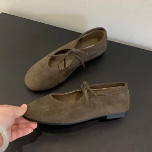 Detail view of brown suede flat ballet shoes with delicate strap bow, soft sole design.