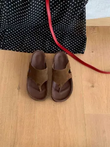 Detailed view of brown suede thong sandals on wooden floor with polka dot background.