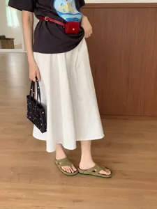 Detailed shot of green suede thong sandals paired with white skirt, casual summer footwear look.