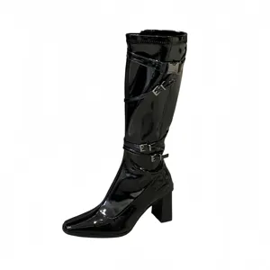 Botas altas de charol negro con tacón ancho, punta puntiaguda y correas con hebilla.