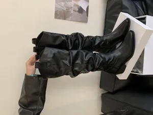 Gros plan de bottes hautes plissées en cuir noir avec bout pointu et talon épais et stylé.
