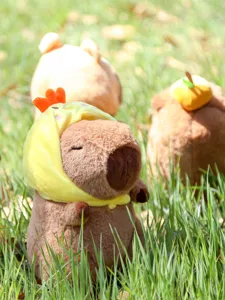 Niedliches Capybara Plüschtier Detail mit weichem gelbem Hühnerhut im Gras draußen.