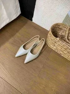 Vue détaillée de chaussures plates pointues blanches avec bride arrière sur sol en bois.