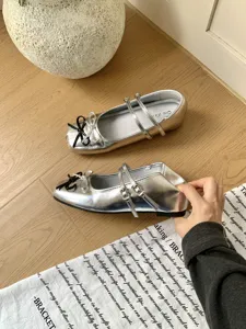 Close up of silver metallic Mary Jane flat shoes with double straps and bow detail.