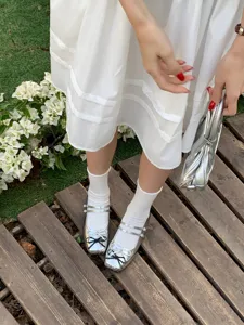 Close-up detail of silver Mary Jane shoes with double straps and black bow, outdoor wooden path scene.