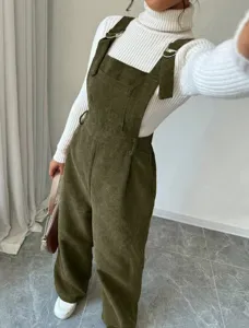 Detailed view of olive green corduroy overalls paired with a white turtleneck sweater.