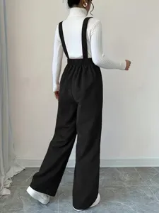 Detail shot of women's black corduroy overalls, loose straight leg pants design, cozy fabric.