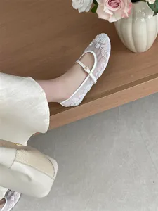 Detail shot of white mesh flat shoes with beaded floral embroidery and buckle strap.