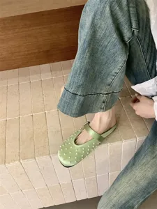 Close-up detail shot of elegant green satin mules featuring delicate pearl embellishments on upper.
