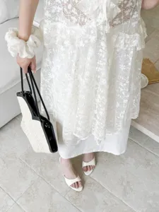 Detail shot of elegant open-toe high heel sandals paired with white lace dress and stylish bag.