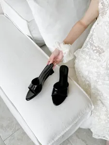 Detail shot of elegant black patent leather open toe wedge mules, showcasing sleek high heels.