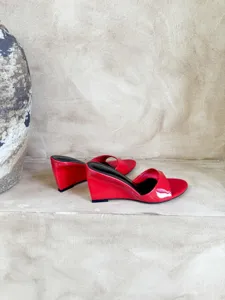 Red patent leather wedge sandal detail, open toe slip-on high heel shoe on rustic shelf.