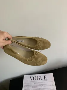 Vista detallada de zapatos planos de ante caqui con un lazo delicado y forro interior suave.