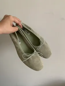 Primer plano de bailarinas de ante verde claro con un lazo y detalles en la plantilla.