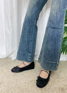 Primo piano di scarpe basse Mary Jane in raso nero con cinturino in strass e fiocco.
