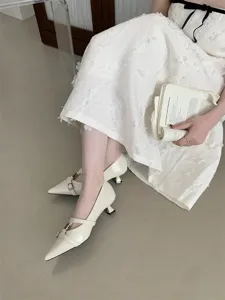 Close-up detail of stylish French retro pointed kitten heels in white with buckle straps.