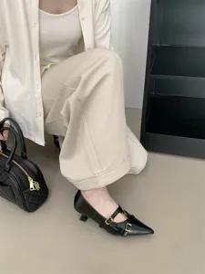 Close-up of elegant black pointed kitten heels with double straps and gold buckles, worn indoors.