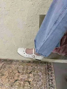 Detaillierte Ansicht weißer flacher Mary-Jane-Schuhe mit zartem Cutout-Design und Riemen.