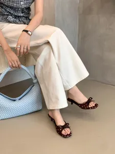 Primer plano de sandalias de mujer con tacón de gatito, lunares y lazo, punta abierta.
