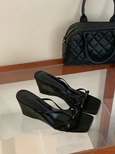 Gros plan de sandales noires à talons compensés, bout carré et brides fines ornées d'un nœud.