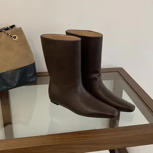 Close-up detail of stylish dark brown square-toe mid-calf boots on glass display table.