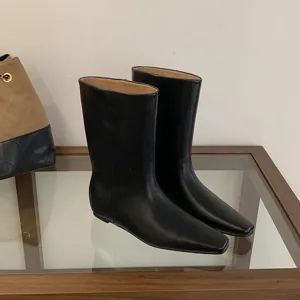 Detail shot of minimalist black square toe mid-calf boots on glass table, elegant design.