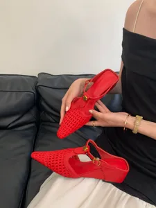 Detalle de mules slingback rojas tejidas de punta, tacón bajo de cuña con hebilla floral.