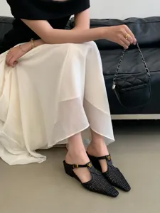 Detalle de zapatos mules negros trenzados de punta, calzado elegante con tacón de cuña.