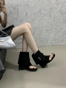 Detailed view of black suede peep-toe wedge sandals with metal buckle and Roman style.