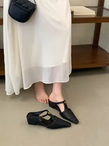 Vista detallada de mules negros trenzados con tacón de cuña y punta afilada, elegantes.