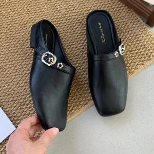 Detailed view of women's black square toe low heel mules with metal buckle decoration.