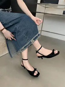 Detailaufnahme von schwarzen Slingback-Kitten-Heels mit Schleife, Knöriemen und offener Spitze.
