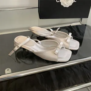Detailansicht eleganter weißer Satin-Kitten-Heel-Sandalen mit schicker Schleife und Riemen.
