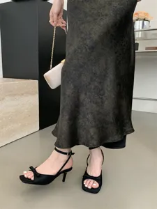 Nahaufnahme eleganter Damen-Sandaletten mit filigranem Stilettoabsatz und süßer Schleife.