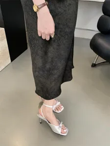 Detailansicht eleganter französischer High-Heel-Sandalen aus Satin mit Schleife und Knöchelriemen.