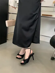 Detailansicht eleganter schwarzer Satinstilettos mit Schleife und feinem Knöchelriemen.