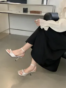Detailaufnahme französischer Schleifen-Stiletto-Sandaletten, weiße Satin-Riemchensandalen offen.
