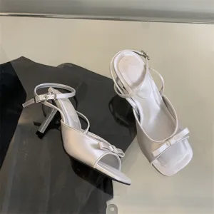 Nahaufnahme Detail silberner Satin High-Heel-Sandalen mit Schleife und Knöchelriemen.