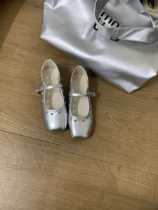 Nahaufnahme silberner Mary-Jane-Flats mit Cutout-Design auf Holzboden präsentiert.