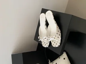 Primer plano de sandalias de tacón bajo con lunares blancos y un lazo cuadrado elegante.