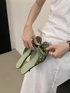Detalle de sandalias de tacón bajo con lunares verdes y lazo, con elegante puntera cuadrada.